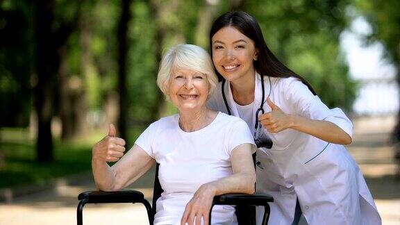 护士和老年残疾妇女对着镜头微笑并显示拇指向上的手势
