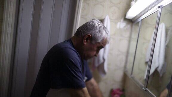 烦恼的老人看着浴室镜子遭受精神疾病