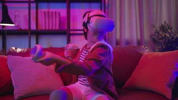亚洲男孩戴着VR或虚拟现实眼镜头戴式站在家里的电视机前玩视频游戏在隔离期间的技术和创新概念霓虹灯夜的生活方式