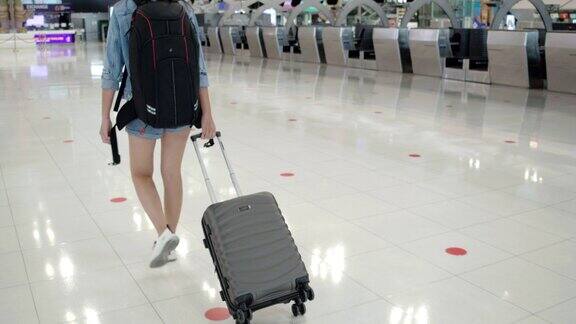 穿着蓝色牛仔裤的亚洲女乘客拖着带轮子的行李箱进入客运大楼