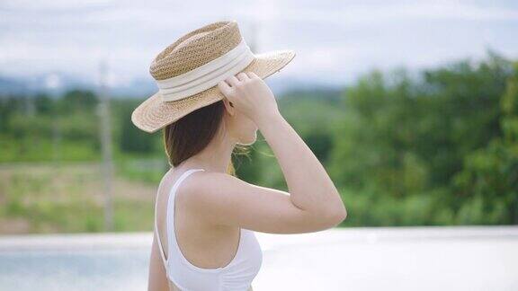 侧面的女人穿着泳衣和夏天的帽子走在泳池边