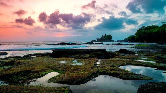 夕阳在破碎的海滩上流逝在远处人们可以看到印尼巴厘岛上的塔纳洛特神庙