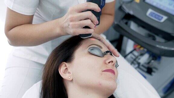 近距离美容师在诊所给年轻女性脸部做激光脱毛手术慢动作