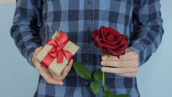 情人节、生日或国际妇女节男人手里拿着礼物和红玫瑰用牛皮纸和蝴蝶结包装的礼盒男性的手节日礼物