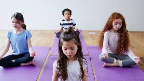 一群孩子坐在运动垫上在瑜伽室里冥想