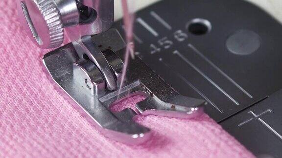 在缝纫机上缝制粉红色材料缝纫机上移动的针的特写