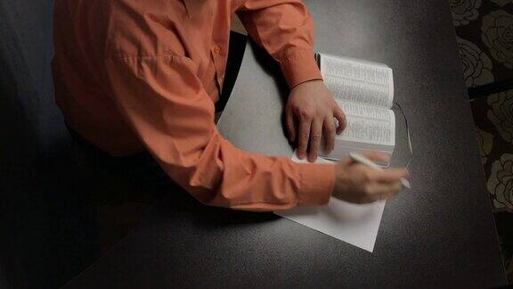 一个人坐在桌子旁读圣经引导手指沿着线把重要的想法写在一张纸上