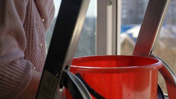 在公寓里擦窗户红色水桶的特写站在梯子上