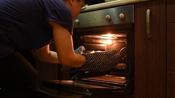 一位亚洲华人中年妇女从厨房的烤箱中取出蛋糕托盘准备做饭