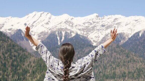 一位年轻女子在一座白雪覆盖的高山前举起双臂