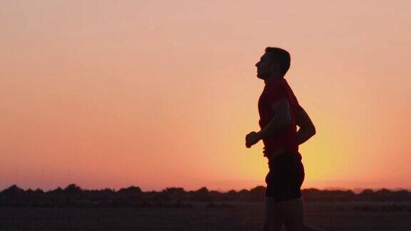 日落时分一个年轻的运动员在海滩上慢跑