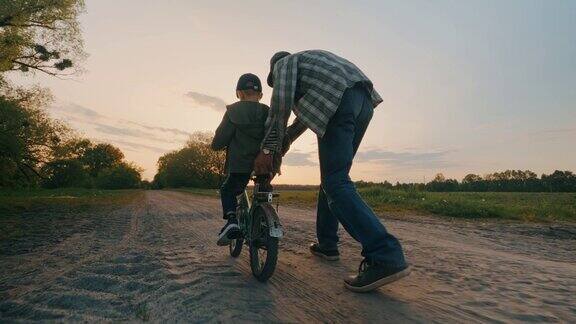 日落时分爸爸教儿子在田野路上骑两轮自行车