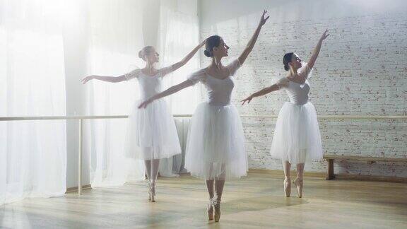 三个年轻和华丽的芭蕾舞者同步跳舞他们穿着白色的芭蕾舞裙拍摄于一个阳光明媚的早晨在一个宽敞明亮的工作室