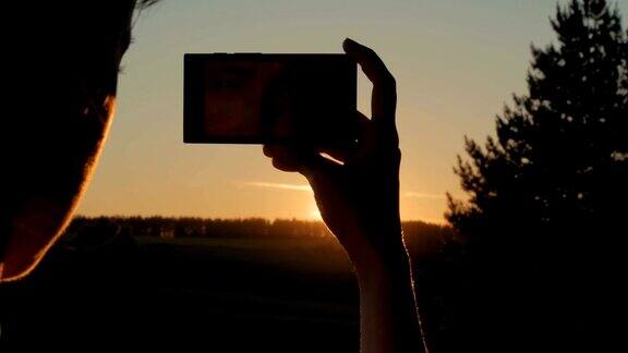 女人用智能手机拍摄日落剪影