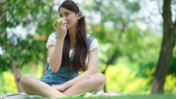 美丽迷人的女人坐在花园与模糊的背景阳光明媚的日子女孩拿着青苹果吃快乐在假期放松香薰自由感受生活方式