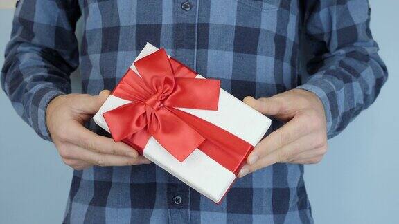 在情人节或生日这天男性的手正在展示带有红色丝带蝴蝶结的礼盒男人拿着系着蝴蝶结的礼物在手里摇晃着圣诞节的节日礼物