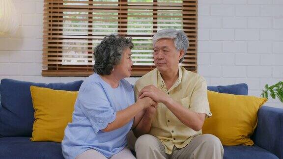 年长的亚洲女人坐在家里客厅的沙发上安慰抑郁的男人退休的人情绪激动