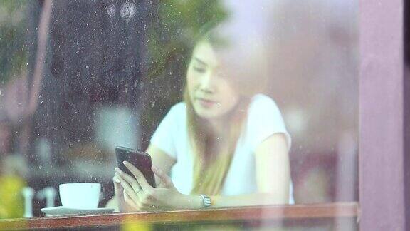 年轻女子在餐厅里用智能手机透过窗户看外面