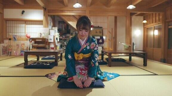 穿着Furisode和服的年轻女子坐在高跟鞋上在日本的榻榻米房间鞠躬