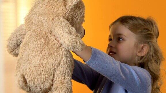 可爱的学龄前女孩看着泰迪熊拥抱它最喜欢的玩具孩子