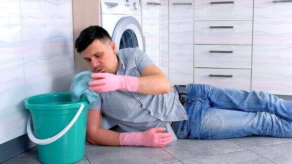 戴着橡胶手套的疲惫男子在打扫完厨房地板后休息了一下