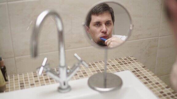 一个男人在盥洗室的小圆镜里刷牙