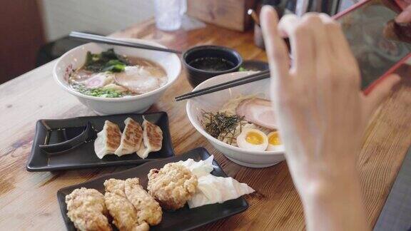 亚洲妇女在日本餐厅用手机拍拉面和日本食物