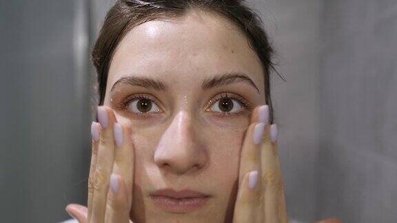 洗脸-一个女孩在看镜头的时候在她的皮肤上涂抹泡沫天然来源的天然化妆品