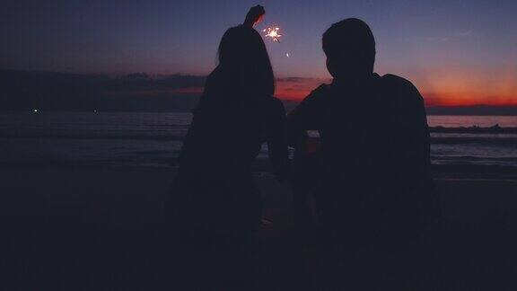 背影剪影的年轻夫妇坐在和放松在海滩上日落