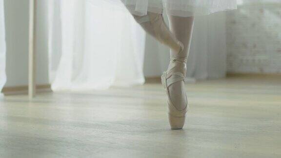 特写镜头的芭蕾舞女演员的腿她穿着芭蕾舞鞋跳舞她穿着白色芭蕾舞裙在阳光明媚的现代工作室拍摄在缓慢的运动