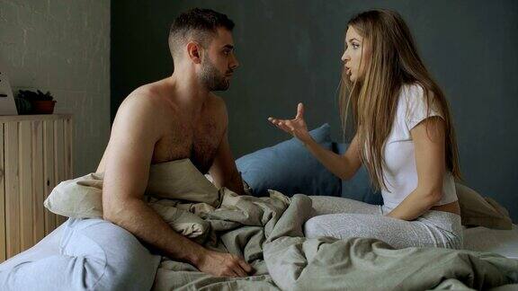 心烦意乱的年轻夫妇坐在床上心烦意乱地争吵着