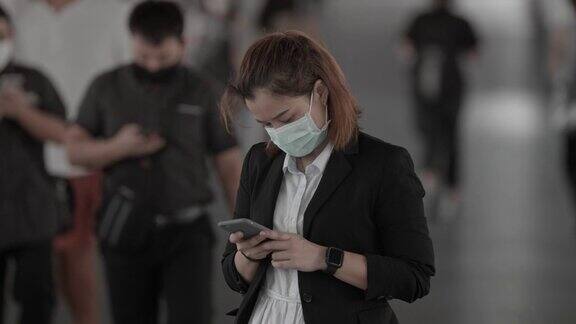 商业女性戴着保护面罩站在人群中使用智能手机慢镜头