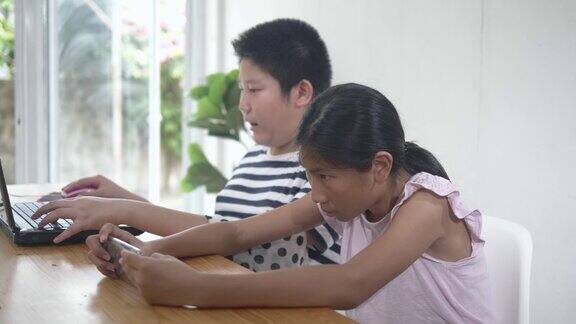 快乐的亚洲男孩和女孩一起玩网络游戏的笔记本电脑和智能手机在家里生活理念