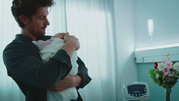 快乐的父亲抱着熟睡的新生儿在病房里
