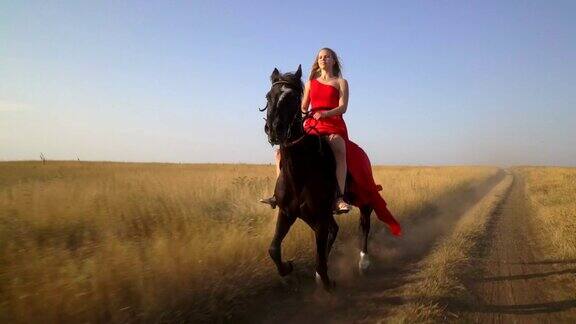 骑马的漂亮姑娘穿着红裙子骑马穿过干燥的草地