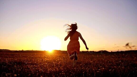 日落时分快乐的女孩在草地上奔跑