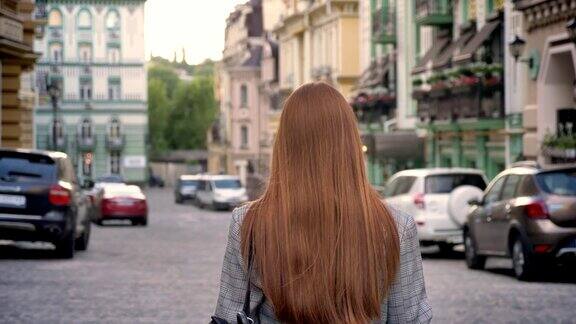 一个留着姜黄色长发的年轻女子背着双肩背包走在城市里城市街道的背景背影