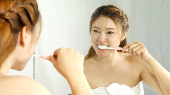 一个穿着浴巾的女人在浴室里用镜子刷牙