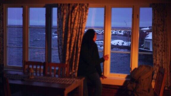 在罗浮敦群岛的一间小木屋里一名女子透过窗户眺望