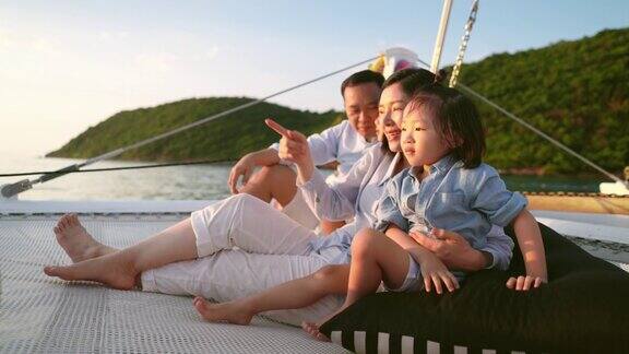 幸福的家庭享受他们的航行他们坐在蹦床上享受着日落时的谈笑风生年轻的父母正试图给他们的儿子指出日落时的美丽风景享受暑假