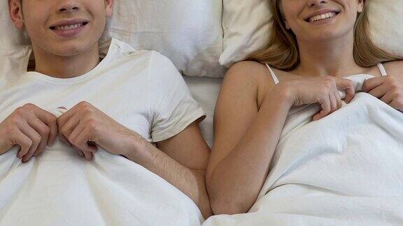 微笑的男友和女友在酒店的床上盖着毯子度蜜月