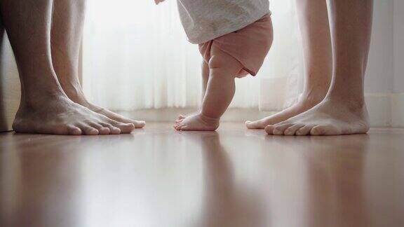 亚洲父母牵着孩子的手学习在家里的木地板上走路可爱的蹒跚学步享受与家人的第一步