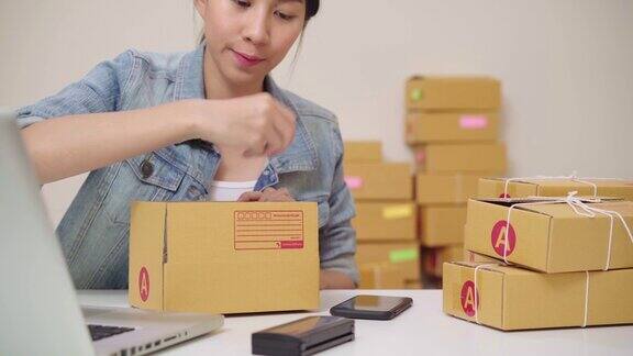 美丽聪明的亚洲年轻企业家女企业主中小企业网上检查产品库存和包装放在盒子在家里工作小企业主在家办公