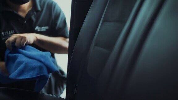 在汽车详细清洁服务期间一位年轻人在清洁座椅坐垫时使用精细的布对汽车内部进行深层清洁