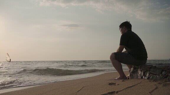 亚洲男人沮丧地独自坐在海滩上