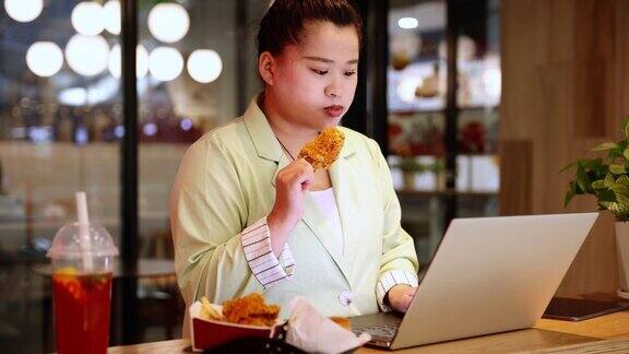 女商人一边用笔记本电脑工作一边吃炸鸡