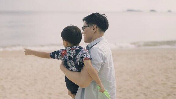 亚裔父亲抱着儿子在海滩上散步