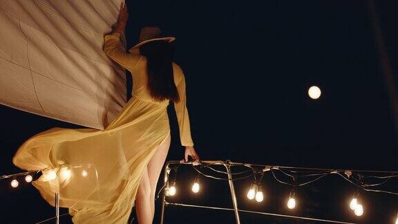 穿着黄色长裙的女人走在夜晚航行的帆船的甲板上