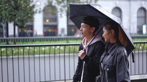 近距离拍摄一对年轻夫妇撑着伞走在下雨的街道上