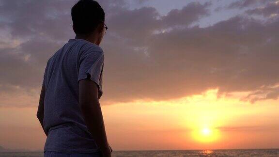 抬起头看美丽的日落和大海的亚洲男人
